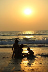 Silhouette siblings playing in sand at beach