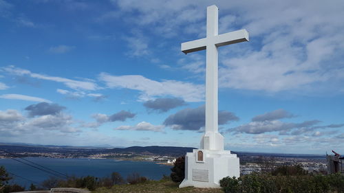 Cross on beach by building against sky