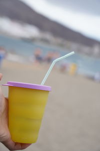 Midsection of person holding drink at beach