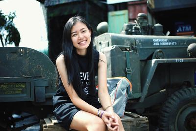 Portrait of smiling young woman sitting against land vehicle