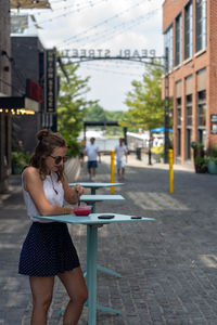 Fashionable woman eating food while standing on footpath
