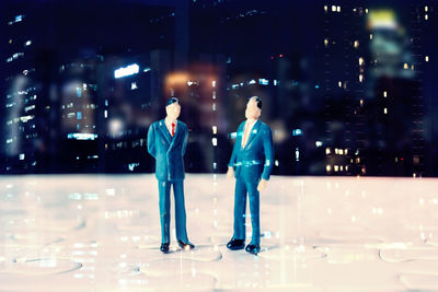 Double exposure of businessman figurines on jigsaw puzzle with buildings at night