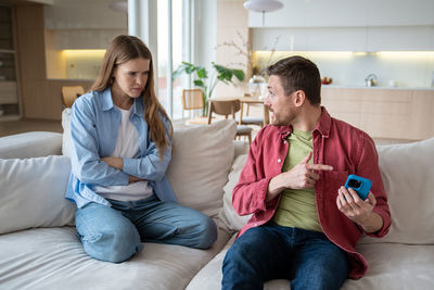 Annoyed wife listening explanations of cheater husband hiding phone display, concealing information