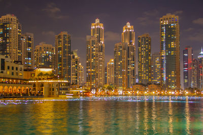 Illuminated buildings by river against sky in city at night