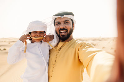 Portrait of father and son doing selfie while standing at desert