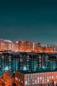 Illuminated buildings in city against clear blue sky