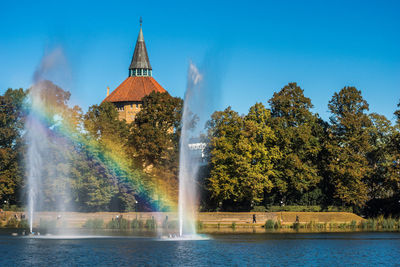 View of a fountain by lake against sky and a rainbow between 