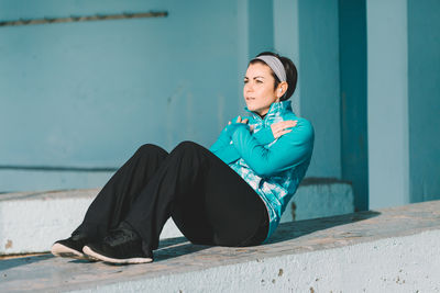 Mid adult woman exercising on railing against turquoise wall