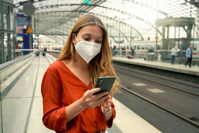 Young woman with protective face mask using mobile phone at berlin central station, germany