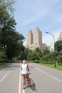 Rear view of woman with bicycle at central park against sky