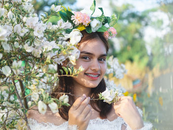 Portrait of smiling young woman against white flowering plants