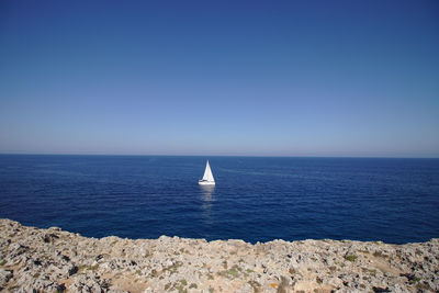 Sailboat in sea against clear blue sky