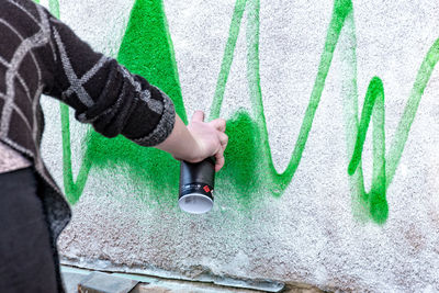 Cropped hand of person painting with spray on wall