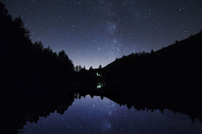 Reflection of silhouette trees in lake against sky at night