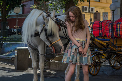 Young woman standing next to horse carriage on the street