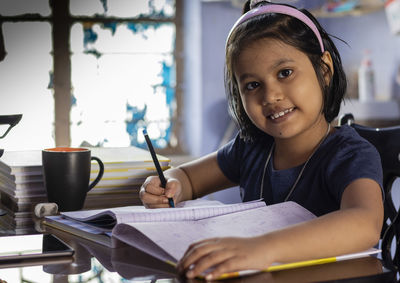 An indian cute girl child studying at home with smiling face