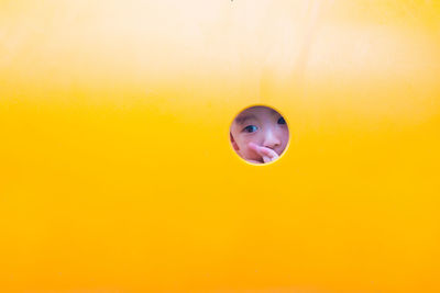 Cute boy looking through hole in yellow playground equipment