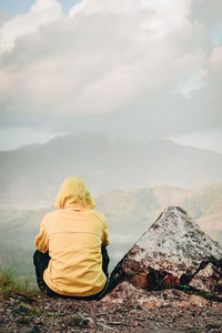 Rear view of man looking at mountain range against cloudy sky