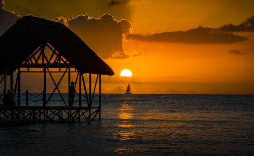 Silhouette person in gazebo fishing by sea during sunset