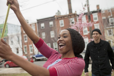 Portrait of smiling young woman with arms raised in city