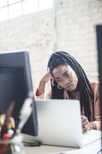 Thoughtful female programmer looking at laptop while working in office