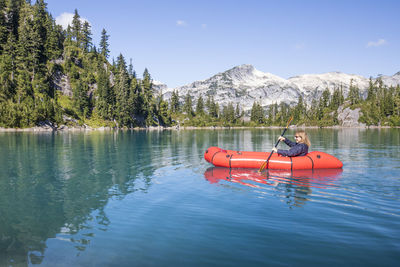 Retired woman paddling red boat on remote lake during a trip.