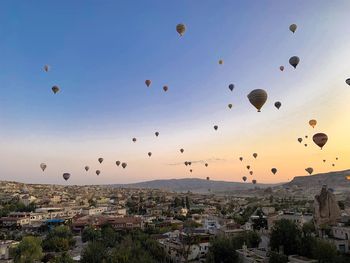 Hot air balloons flying in city against sky during sunset