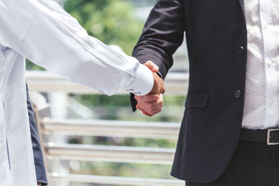 Midsection of colleagues handshaking on elevated walkway