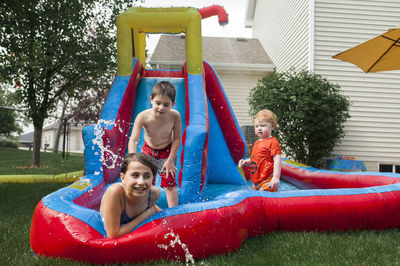 Siblings playing in inflatable water slide at backyard