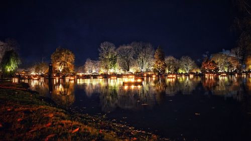 Illuminated trees by river against sky at night