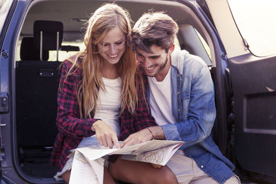 Smiling friends using laptop while sitting in car