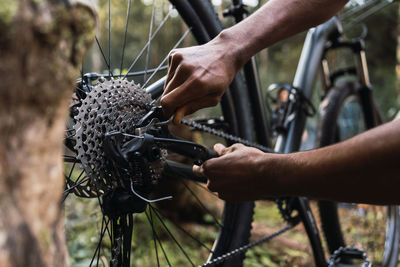 Cropped male cyclist fixing mechanism of bicycle against hiker setting in forest