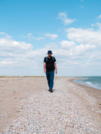 Bearded millennial man in bucket hat walking on empty beach. authentic hipster  outdoor solo travel 