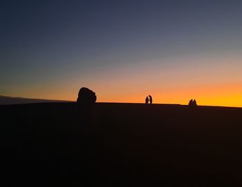 Silhouette people on rock against sky during sunset