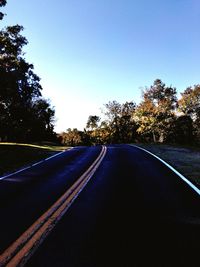 Road amidst trees against clear blue sky