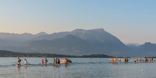 People in lake garda against mountains at san giorgio maggiore
