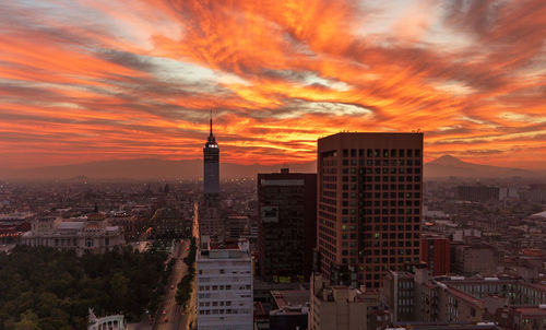 Buildings in city against romantic sky at sunset