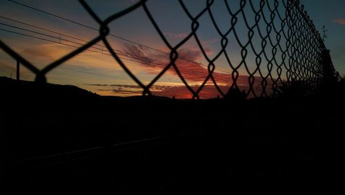 Close-up of silhouette chainlink fence against sky