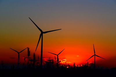 Silhouette wind turbines on field against sky during sunset