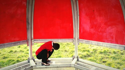 Full length of boy crouching at red gazebo at park