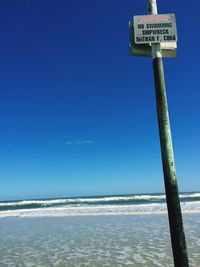 Warning sign on sea against blue sky