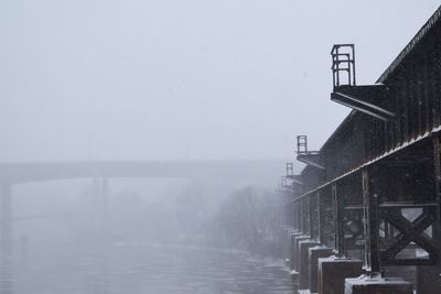 Low angle view of bridge by river against clear sky during snowfall