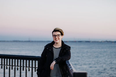 Portrait of smiling young woman standing by sea against clear sky