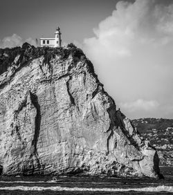 Lighthouse on cliff by sea against sky