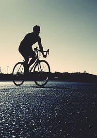 Silhouette man riding bicycle on road against clear sky