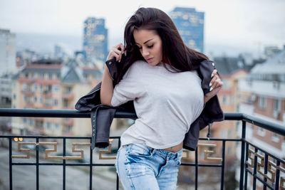 Beautiful young woman wearing sunglasses and jacket standing in balcony