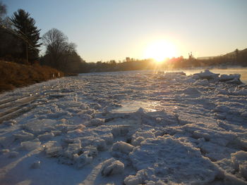 Snow covered landscape against sky during sunset