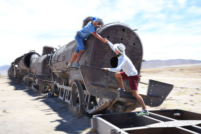 Man helping friend while climbing in abandoned train at desert