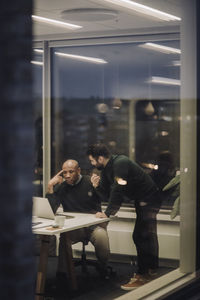 Businessman discussing with male colleague over laptop at work place