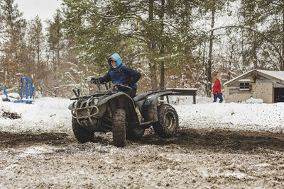 Teenage boy riding quadbike while girl walking on snow covered field during winter